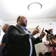 Alex jones stands in the center with both fingers up talking to reporters. His attorney Antonio Reynal stands behind him.